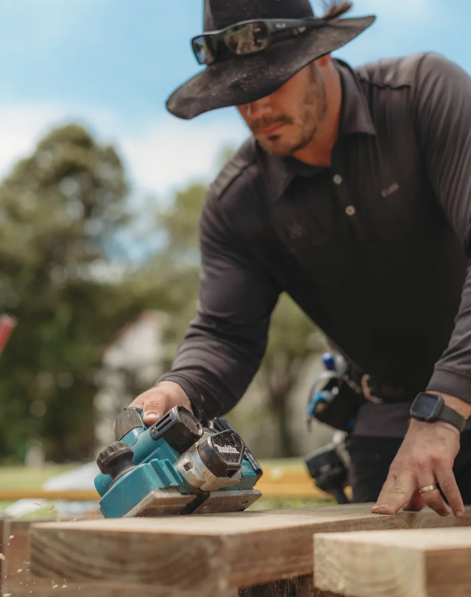 Evan working on-site with a hand planer, smoothing a timber paling